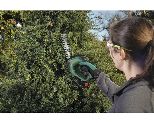 Kvinna klipper häck med sladdlös häcksax