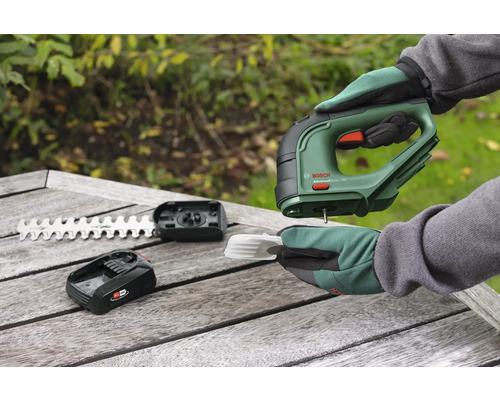 Batteridriven grässax med batteri, kniv och tillbehör på ett träbord