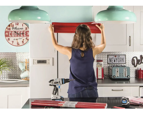 Kvinna fäster möbelfolie i köket. I förgrunden en sladdlös skruvdragare och folierullar.