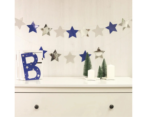 Dekorativ scen med stjärngirlang, dekorativ bokstav, julgranar och ljus på en byrå