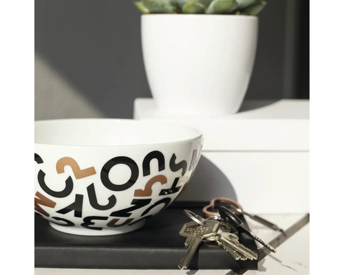 Dekorativ skål med bokstavsmönster bredvid nyckelknippa och krukväxt