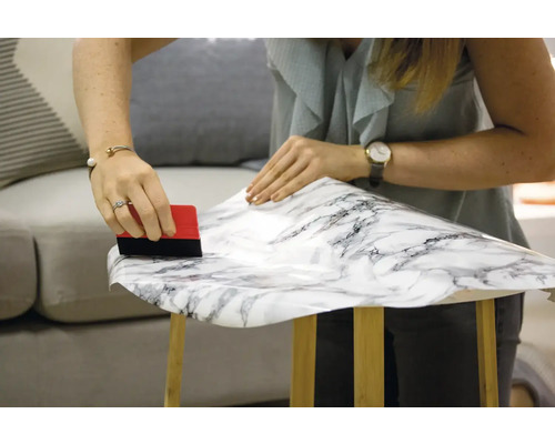 Kvinna applicerar dekorativ folie med marmormönster och skrapa på bord