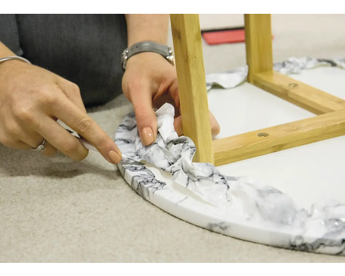 En person skär av film med en kniv från ett runt bord med ben av bambu