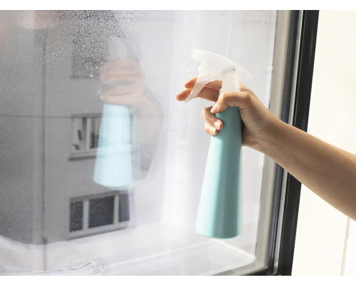 Hand som sprayar fönster med rengöringsmedel