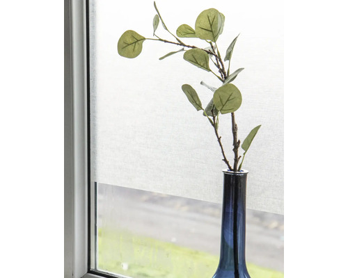 Dekorativa grenar i en vas framför ett fönster med rullgardin