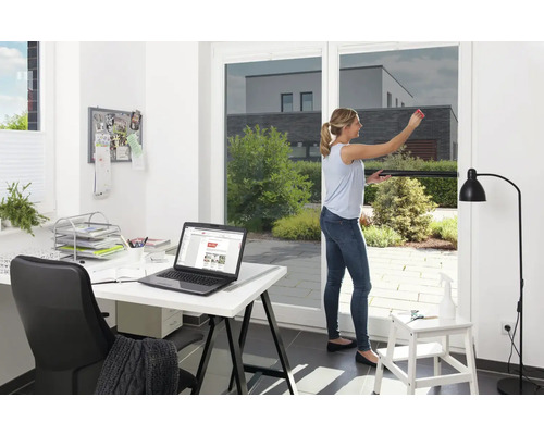 Kvinna applicerar solskyddsfilm på fönstret, kontor i bakgrunden