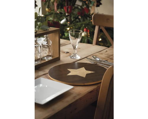 Festligt dukat träbord med tallrik, bestick, glas, bordstablett och julgran i bakgrunden