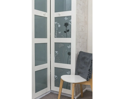 Vitt skåp med blommönster och glasdörrar bredvid en stol med en grå filt