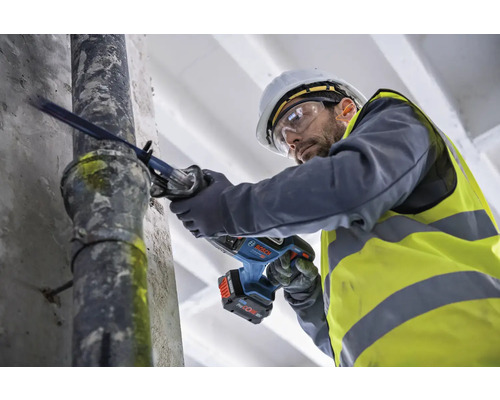 En man med skyddshjälm och skyddsglasögon sågar ett rör med en tigersåg.