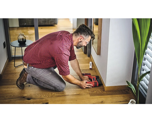 Man fäster golvlister på en vägg med en elektrisk häftpistol