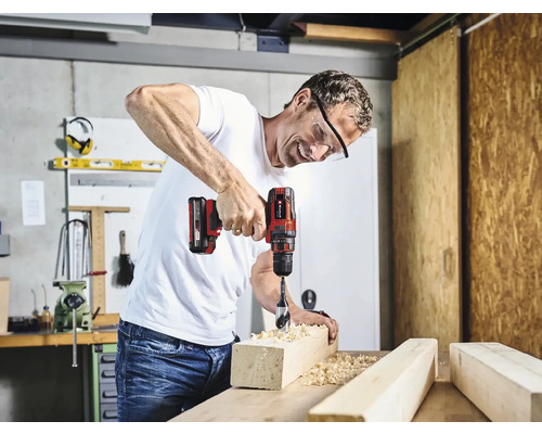 En man borrar med en sladdlös skruvdragare i en träbit i en verkstad.