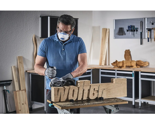 En man slipar en bit trä med inskriptionen Wolter med en slipmaskin.