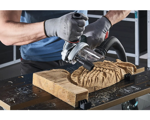 En hantverkare bearbetar en träbit med en handöverfräs på en arbetsbänk.