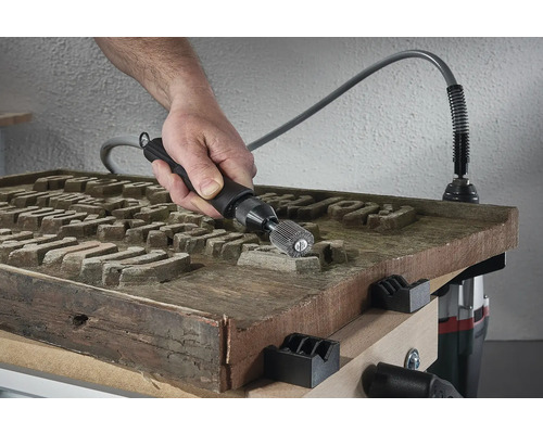 Hand med slipverktyg bearbetar träskiva med gravyr på en arbetsbänk