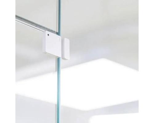 Vit fönster- eller dörrkontaktsensor fäst på en glasskiva