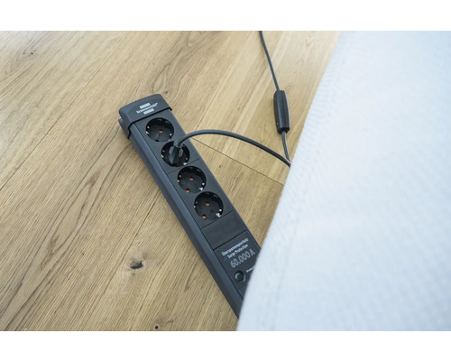 Grenuttag med överspänningsskydd och ansluten kontakt på ett trägolv