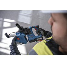 En arbetare håller en blå borrhammare från Bosch med ett 18 volts batteri.