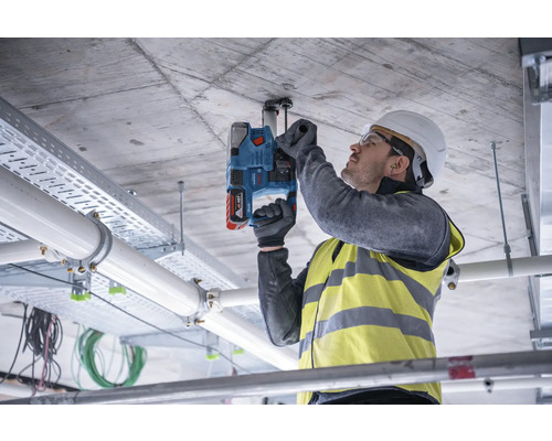 En man borrar i ett betongtak med en slagborrmaskin för att fästa en fästanordning.