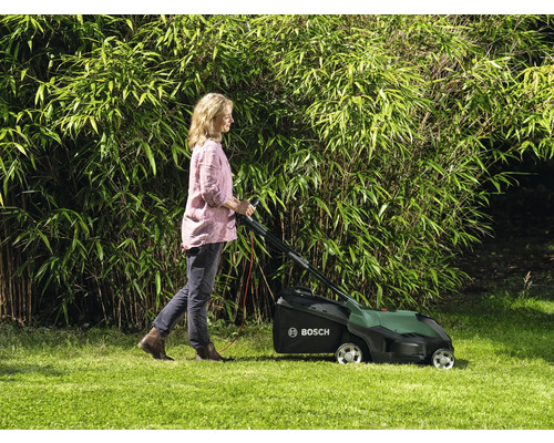 Kvinna använder gräsklippare i trädgården