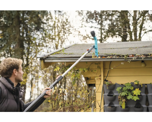 En man rengör en takränna med ett teleskopiskt handtag.