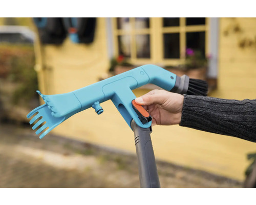 Gardena Cleansystem trädgårdsredskapsrengörare med borste och skrapa hålls av en person.