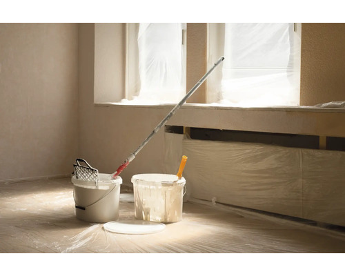 Rum med färgburkar, roller och täckfilm för renovering