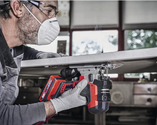 En man använder en sladdlös sticksåg för träbearbetning, skyddsglasögon och ansiktsmask används.