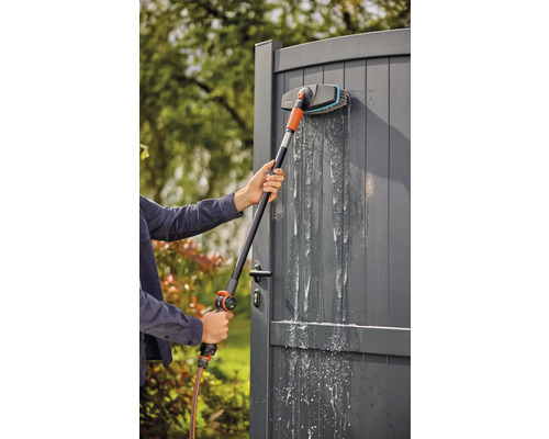 Person rengör en grå trädgårdsport med en tvättborste och vattenslang.