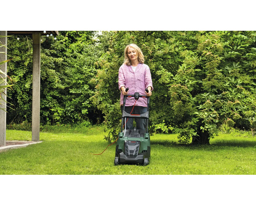 Kvinna använder en gräsklippare i trädgården.