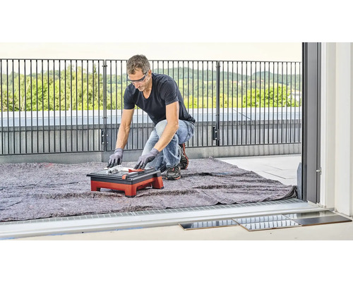 En man skär kakel med en kakelskärare på en balkong.