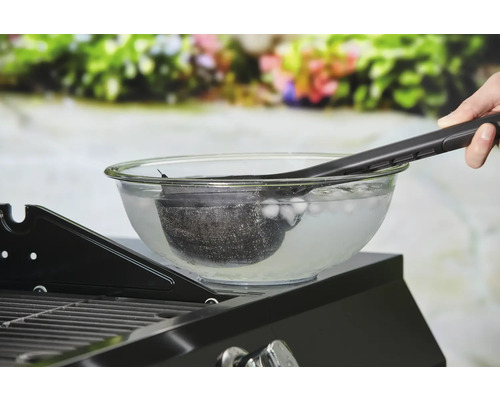 Rengöring av en grillkorg i en skål med isvatten med grilltång.