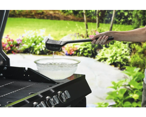 Person rengör grillgaller med grillborste över en skål med vatten.