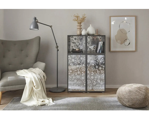 Vardagsrumsscen med fåtölj, golvlampa, matta, pall och hylla med blommönster