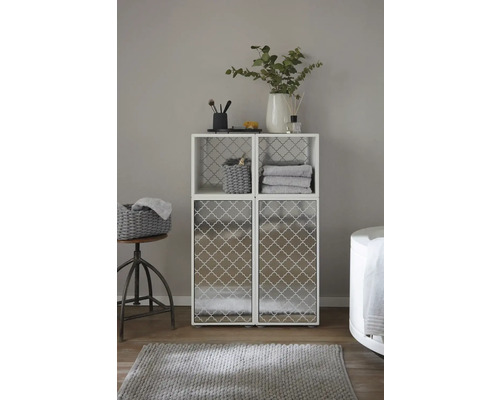 Badrumsscen med ett vitt hyllsystem med två övre fack och två nedre skåpdörrar, dekorerat med badrumsartiklar och textilier