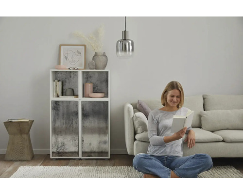 Vardagsrum med hyllor, dekoration, pendellampa, soffa och en kvinna som läser en bok.