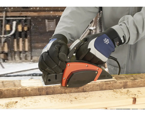 En person hyvlar en träplanka med en elektrisk hyvel utomhus.