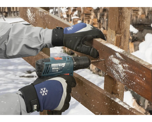 En person borrar ett hål i en träbräda med en sladdlös skruvdragare medan han bär handskar