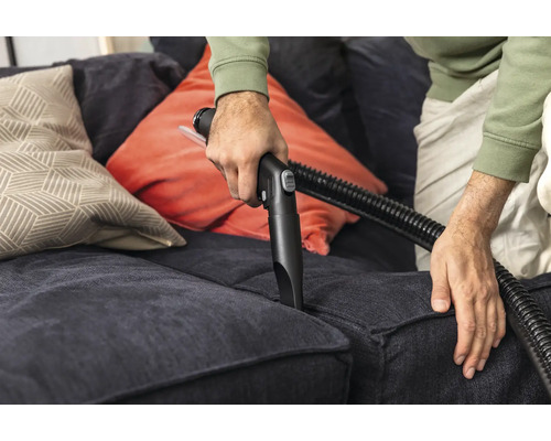 Person rengör soffa med dammsugarmunstycke