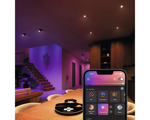 Översikt över ett vardagsrum med taklampor, trappa och en smartphone-app för ljusstyrning.