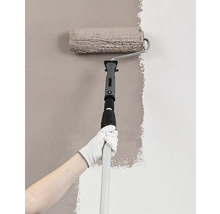 Person målar vägg med färgroller och teleskopstång