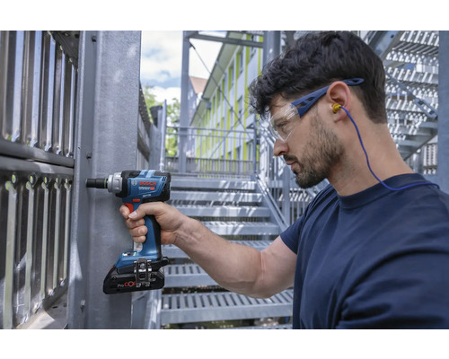Hantverkare med skyddsglasögon och hörselskydd arbetar med en sladdlös mutterdragare på en metallkonstruktion.