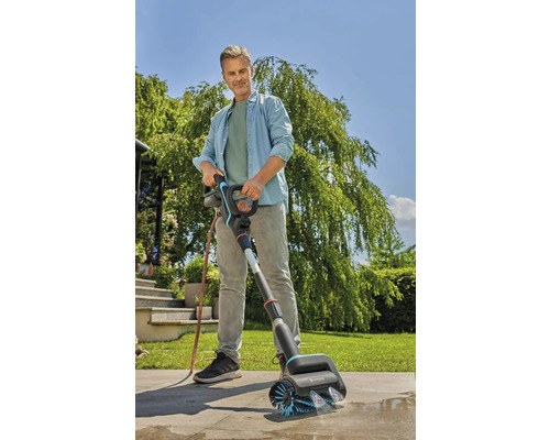 En man använder en Gardena-borste för att rengöra en terrass.