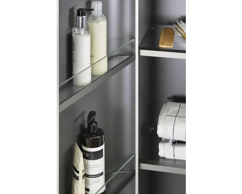 Detaljvy av ett badrumsskåp med glashyllor och diverse badrumsartiklar som handdukar, borstar och hygienprodukter.