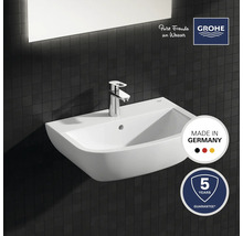Keramisk tvättställ med armatur mot mörk kakelbakgrund, kvalitetsstämpel Tillverkad i Tyskland, Grohe-logotyp, fem års garanti