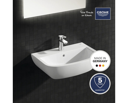 Keramisk tvättställ med armatur mot mörk kakelbakgrund, kvalitetsstämpel Tillverkad i Tyskland, Grohe-logotyp, fem års garanti