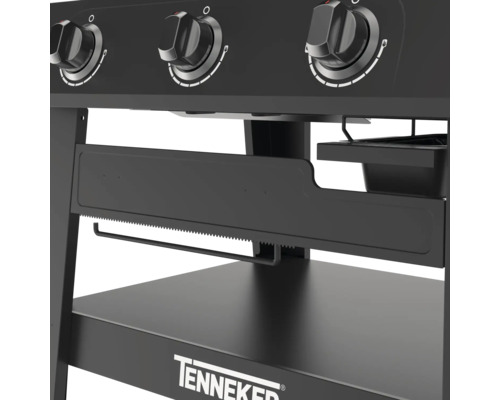 Detaljvy av en svart gasolgrill med vridknappar, pappershanddukshållare och förvaringsyta av märket Tenneker.