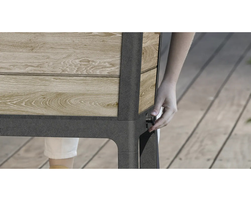 Detaljbild av en upphöjd trädgårdssäng i trä och metall med en person som använder en knapp