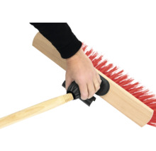 En hand håller en sopborste med träskaft och röd borst.