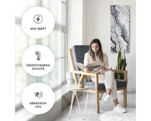 Kvinna läser tidning i ett ljust, modernt rum med en värmepanel på väggen. Symbolerna visar 800 watt effekt, överhettningsskydd och tyst drift.
