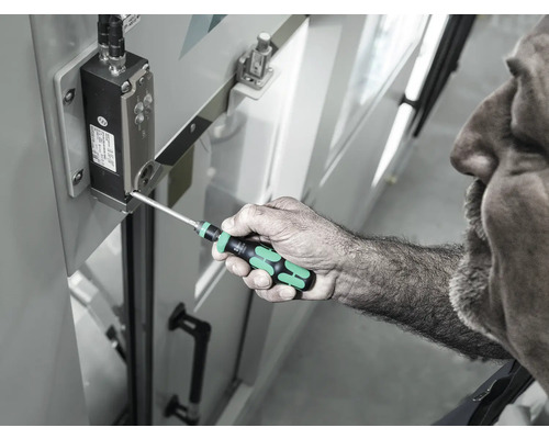 En man använder en skruvmejsel för att dra åt en skruv på en elektronisk komponent.